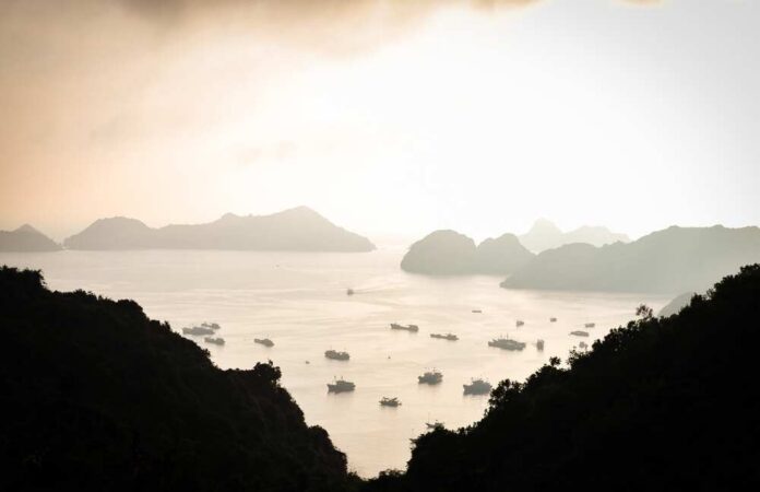 A tranquil view of islands and boats on calm water during sunset