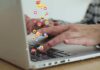 Hands typing on a laptop with floating emojis above