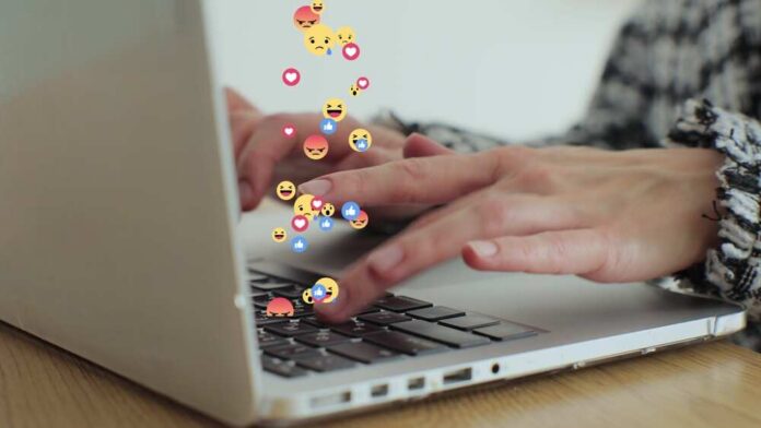 Hands typing on a laptop with floating emojis above