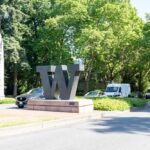 A large 'W' sculpture at a park entrance surrounded by trees