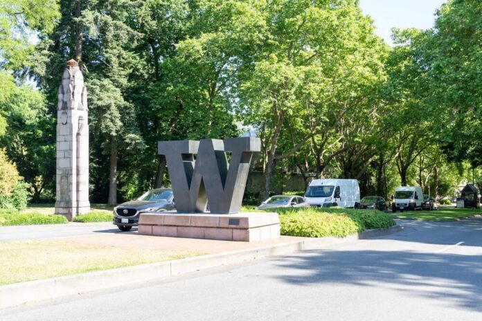A large 'W' sculpture at a park entrance surrounded by trees