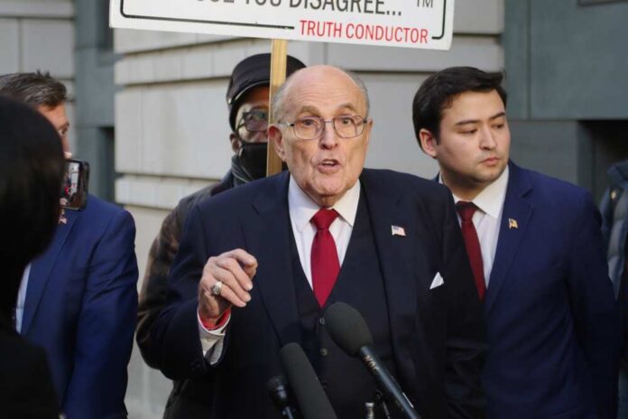 A man speaking at a press conference with a protest sign in the background