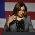 A female politician speaking at a podium with an American flag backdrop