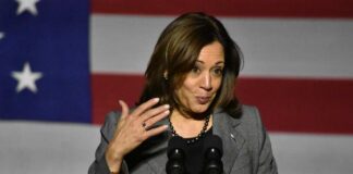 A female politician speaking at a podium with an American flag backdrop
