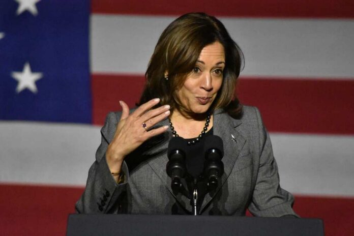 A female politician speaking at a podium with an American flag backdrop