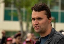 A man passionately speaking at an outdoor event with an engaged audience in the background
