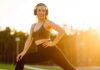 Smiling woman in sportswear wearing headphones, posing outdoors during sunset