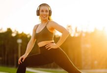 Smiling woman in sportswear wearing headphones, posing outdoors during sunset