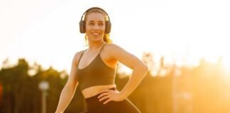 Smiling woman in sportswear wearing headphones, posing outdoors during sunset