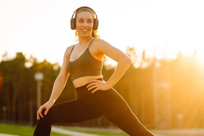 Smiling woman in sportswear wearing headphones, posing outdoors during sunset
