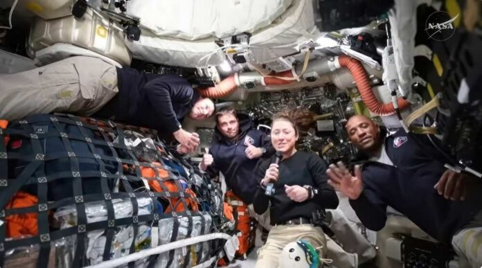 Four astronauts inside a spacecraft, smiling and posing for the camera