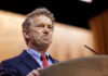 A man in a suit speaking at a podium with a serious expression