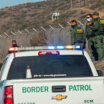 Border Patrol officers speaking with individuals near a fence.