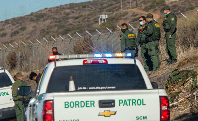 1900868446jpeg-1 Border Patrol officers speaking with individuals near a fence.