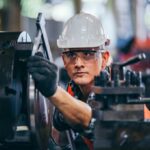 Factory worker adjusting a machine with protective gear