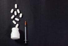 Pills spilled from bottle alongside a syringe