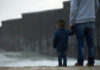 Thousands of Migrant Children, Missing Answers Adult and child standing near border wall beach