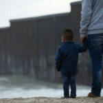 Adult and child standing near border wall beach