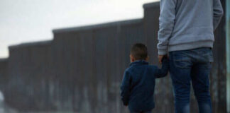 Adult and child standing near border wall beach