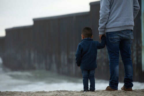 Adult and child standing near border wall beach