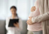 Pregnant person holding their belly during a medical visit