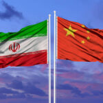 Flags of Iran and China waving against a colorful sky