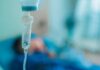 Close-up of an IV drip in a hospital setting with a patient in the background