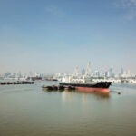 Cargo ships docked in a harbor with a city skyline in the background