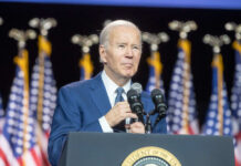 Man speaking at podium with American flags behind.