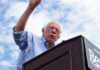 What’s Driving Democrats’ Latest Divide? Man speaking at a podium under cloudy sky.