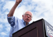 What’s Driving Democrats’ Latest Divide? Man speaking at a podium under cloudy sky.