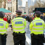 Three police officers in high-visibility jackets stand facing a busy street