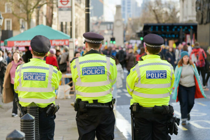 Three police officers in high-visibility jackets stand facing a busy street
