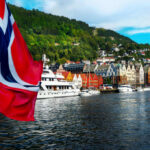 Norwegian flag over harbor with colorful waterfront buildings and boats