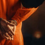 Person in orange jumpsuit with hands cuffed behind back
