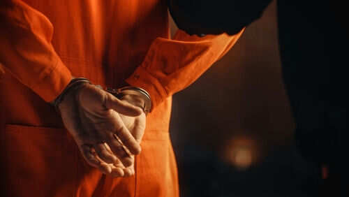 Person in orange jumpsuit with hands cuffed behind back