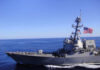 A naval destroyer sailing in the ocean with an American flag