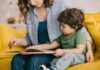 Woman reading a picture book with a young child on a yellow couch