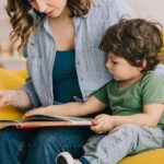 Parenting Has Never Looked More Different Woman reading a picture book with a young child on a yellow couch
