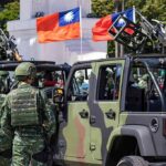 Soldiers beside camouflaged military vehicles with mounted guns and flags