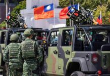 Soldiers beside camouflaged military vehicles with mounted guns and flags
