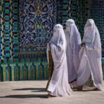 Three women in white veils walking past ornate blue tilework