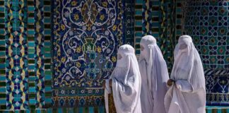 Three women in white veils walking past ornate blue tilework