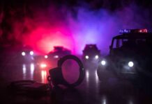 Handcuffs on a surface with police cars and flashing lights in the background