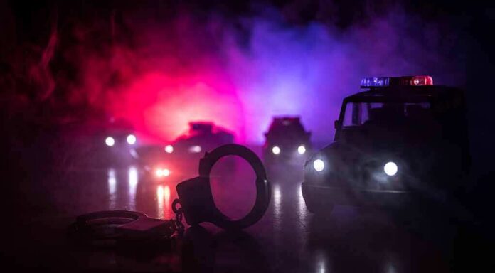 shutterstock_1124703464 Handcuffs on a surface with police cars and flashing lights in the background