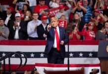 man in suit points from a stage at a political rally