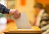 Hand placing a ballot into a wooden voting box