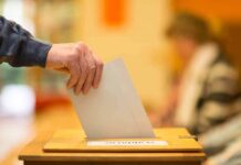 Hand placing a ballot into a wooden voting box