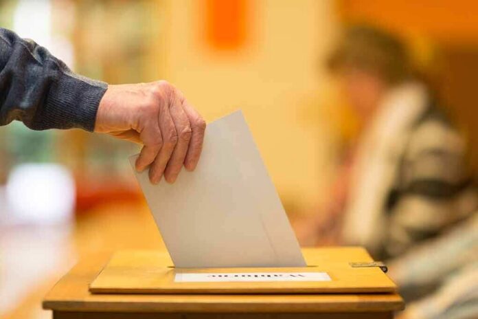 shutterstock_1728981370 Hand placing a ballot into a wooden voting box