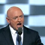 Bald man in suit speaking into a microphone